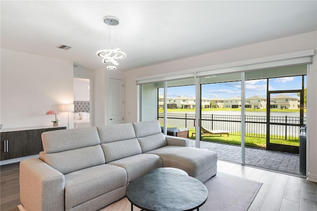 living room with hardwood / wood-style floors, a water view, and a notable chandelier