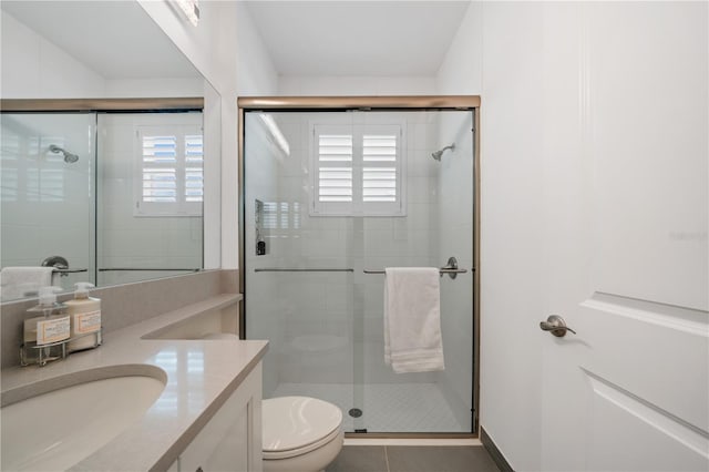 bathroom featuring toilet, tile patterned flooring, vanity, and a shower with door