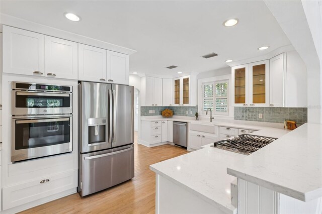106 19th Ave, St Pete Beach, FL 33706 - kitchen with appliances with stainless steel finishes, a peninsula, decorative backsplash, glass insert cabinets, and light wood finished floors