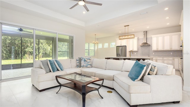 living room with light tile patterned flooring, a raised ceiling, and ceiling fan with notable chandelier