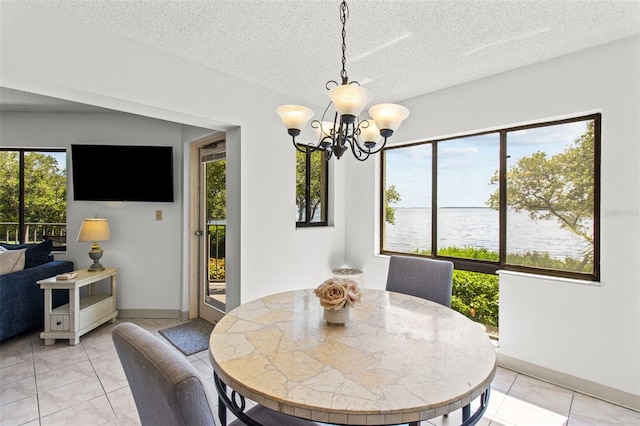 tiled dining space featuring a textured ceiling, an inviting chandelier, and a water view