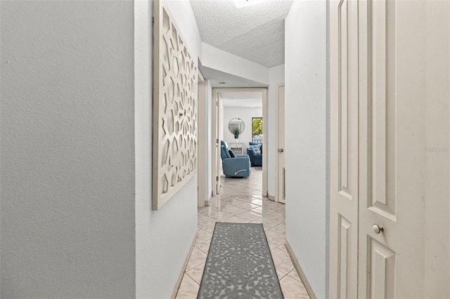 hallway featuring light tile patterned flooring, a textured wall, and a textured ceiling