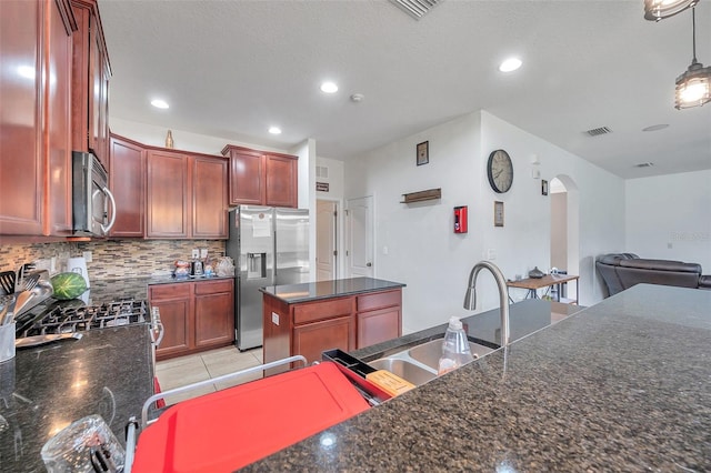 kitchen featuring tasteful backsplash, hanging light fixtures, a kitchen island, appliances with stainless steel finishes, and dark stone countertops