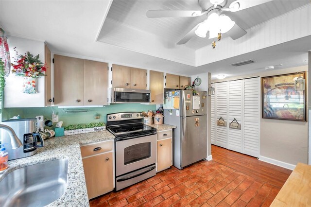 kitchen featuring sink, appliances with stainless steel finishes, light brown cabinets, a tray ceiling, and ceiling fan