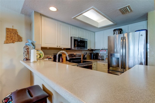 kitchen with appliances with stainless steel finishes, a textured ceiling, white cabinets, and kitchen peninsula