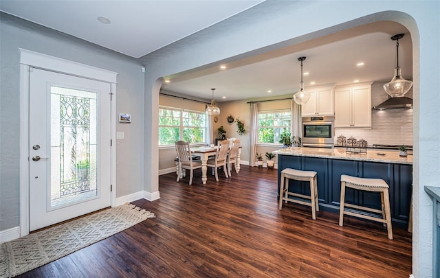 kitchen featuring decorative light fixtures, light stone countertops, dark hardwood / wood-style flooring, white cabinetry, and a breakfast bar