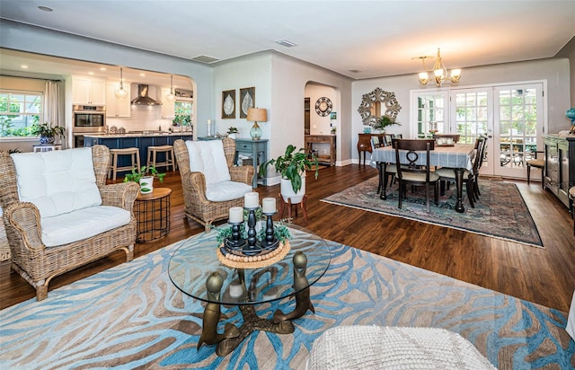 living room with a wealth of natural light, an inviting chandelier, and dark hardwood / wood-style flooring