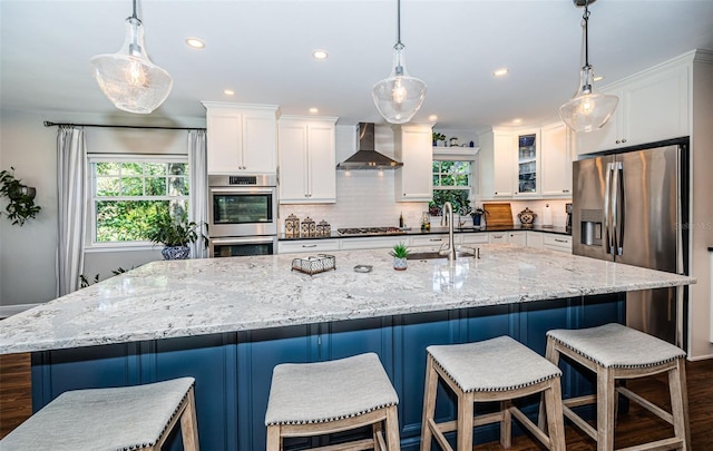 kitchen with wall chimney range hood, a breakfast bar area, stainless steel appliances, and light stone countertops