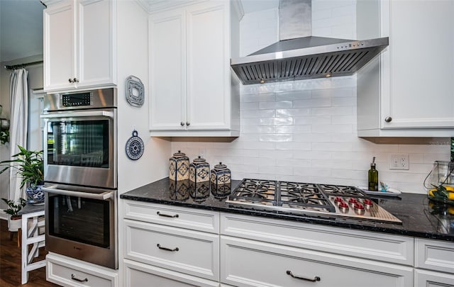 kitchen featuring appliances with stainless steel finishes, wall chimney exhaust hood, white cabinets, and decorative backsplash