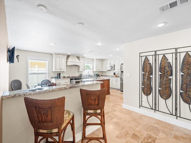 kitchen with a healthy amount of sunlight, custom range hood, a breakfast bar, and appliances with stainless steel finishes