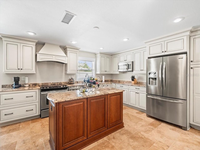 kitchen featuring appliances with stainless steel finishes, light stone counters, premium range hood, and a kitchen island