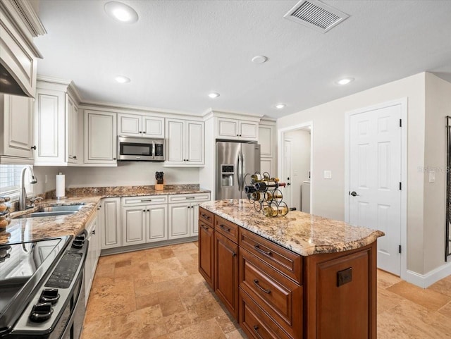 kitchen with white cabinetry, stainless steel appliances, light stone counters, a kitchen island, and sink