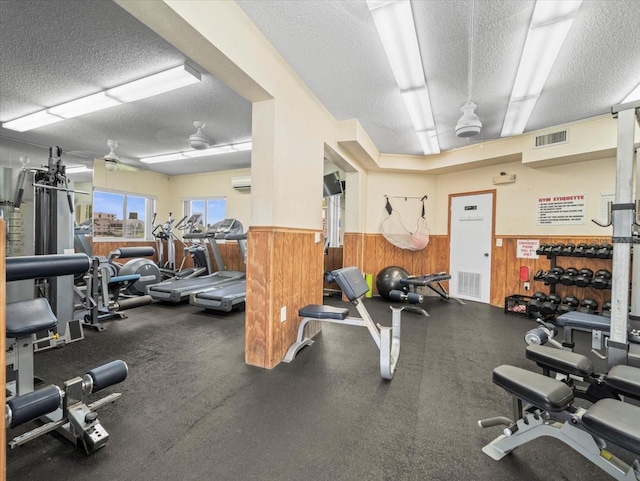 gym featuring wood walls, ceiling fan, a wall unit AC, and a textured ceiling