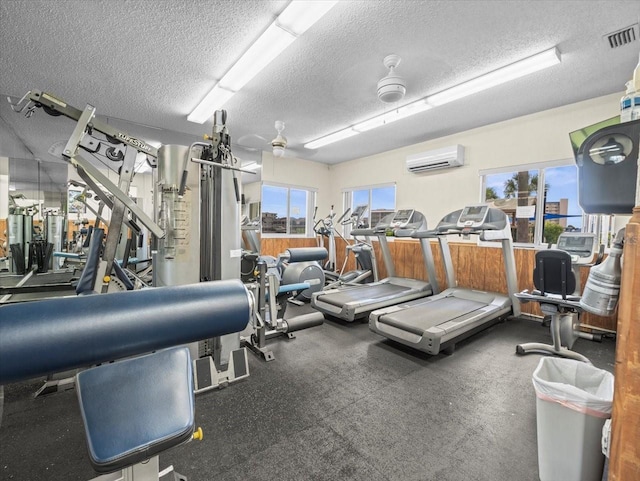 gym with a textured ceiling, ceiling fan, and a wall mounted air conditioner