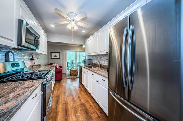 kitchen with sink, appliances with stainless steel finishes, wood-type flooring, tasteful backsplash, and white cabinets