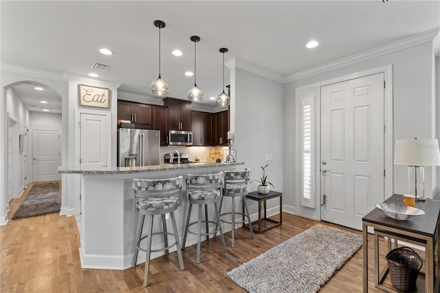 kitchen with ornamental molding, light hardwood / wood-style flooring, appliances with stainless steel finishes, and dark brown cabinets