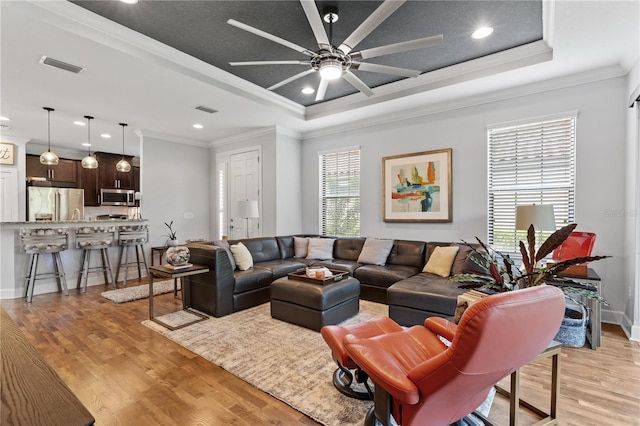 living room with a tray ceiling, ceiling fan, crown molding, and light wood-type flooring