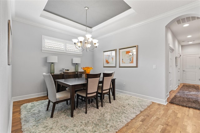 dining space with a raised ceiling, ornamental molding, hardwood / wood-style floors, and an inviting chandelier