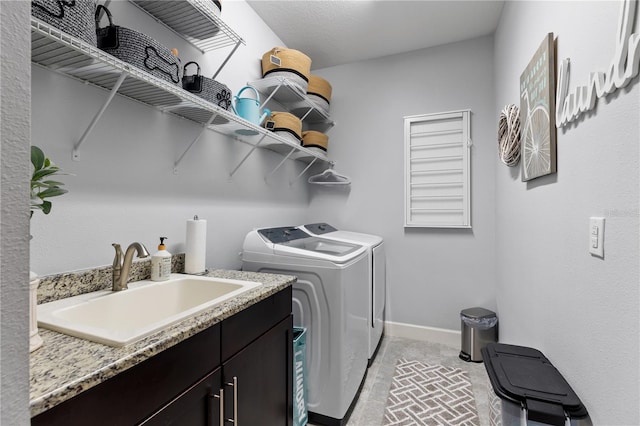 clothes washing area featuring sink, washing machine and dryer, and cabinets