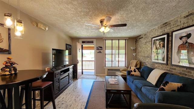 living room featuring ceiling fan, wood-type flooring, brick wall, and a textured ceiling