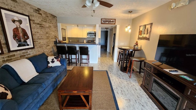 living area featuring ceiling fan, a textured ceiling, brick wall, and light wood finished floors