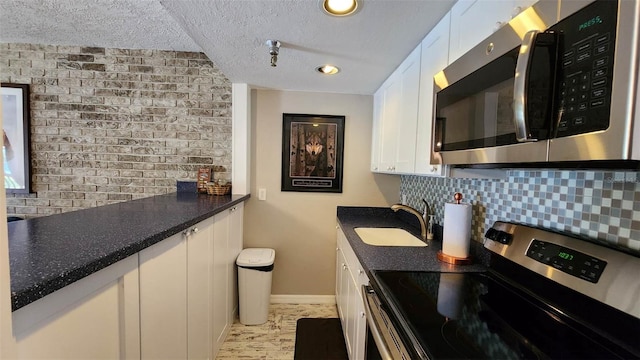 kitchen featuring a sink, white cabinets, appliances with stainless steel finishes, decorative backsplash, and dark countertops