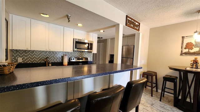 kitchen with stainless steel appliances, dark countertops, a peninsula, and white cabinets