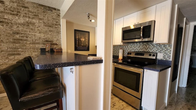 kitchen with a textured ceiling, wood finished floors, white cabinets, appliances with stainless steel finishes, and backsplash