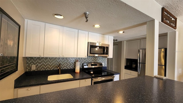 kitchen featuring stainless steel appliances, decorative backsplash, white cabinets, a sink, and a textured ceiling