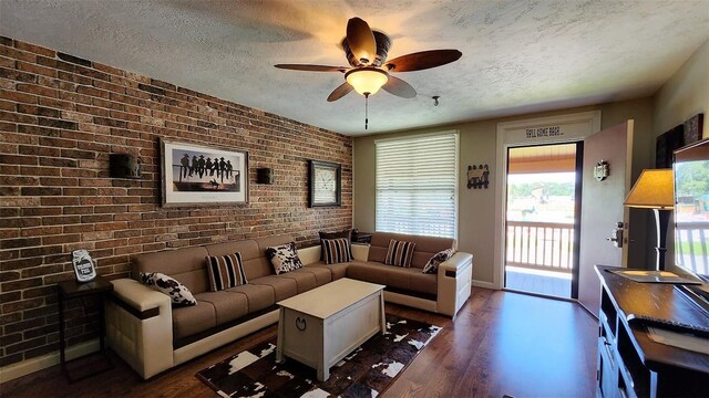 living room with ceiling fan, brick wall, dark wood-type flooring, and a textured ceiling