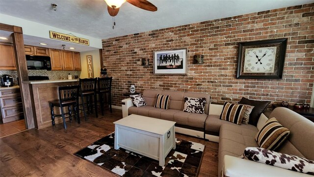 living room featuring dark hardwood / wood-style flooring, brick wall, and ceiling fan