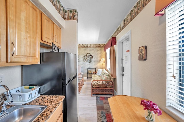 kitchen featuring light brown cabinetry, a brick fireplace, black refrigerator, light wood-type flooring, and sink