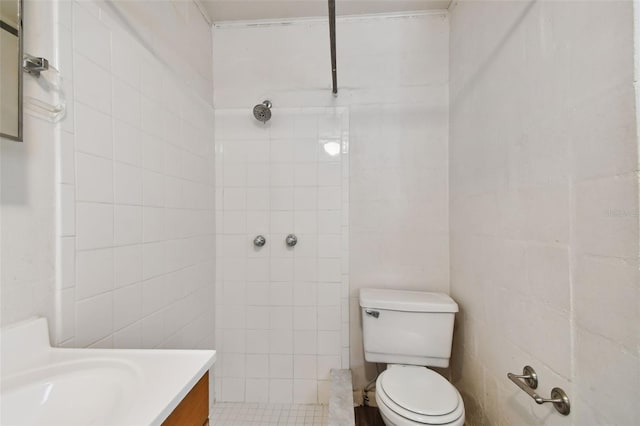 bathroom featuring toilet, vanity, tile patterned floors, tile walls, and tiled shower