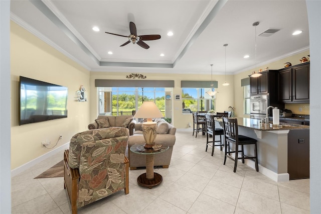 tiled living room with ceiling fan, crown molding, sink, and a raised ceiling