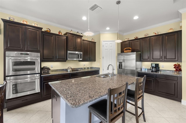 kitchen with a center island with sink, stainless steel appliances, dark brown cabinetry, and decorative light fixtures