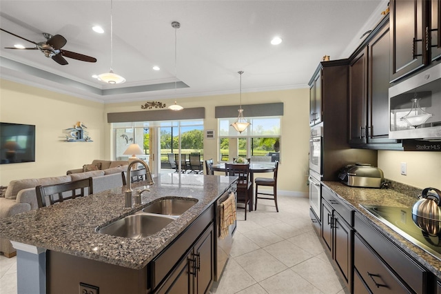 kitchen featuring a center island with sink, stainless steel appliances, a tray ceiling, sink, and dark brown cabinetry