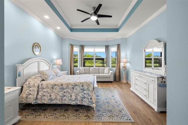 bedroom featuring light hardwood / wood-style flooring, a tray ceiling, crown molding, and ceiling fan