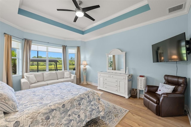 bedroom with ceiling fan, a raised ceiling, ornamental molding, and light hardwood / wood-style floors