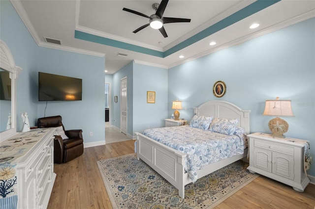 bedroom featuring ceiling fan, light wood-type flooring, crown molding, and a tray ceiling