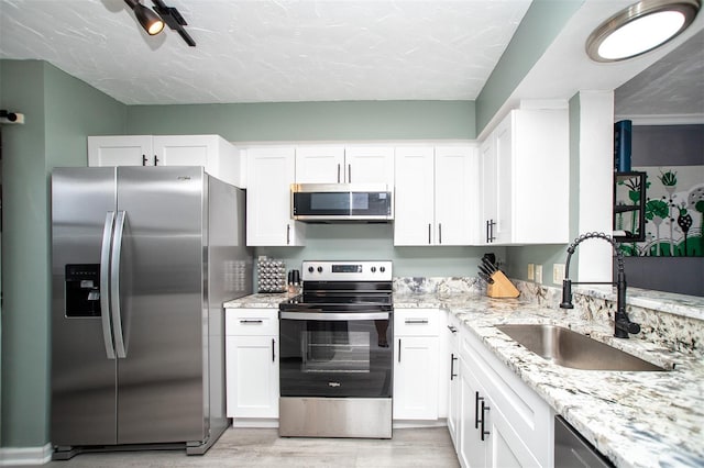 kitchen with white cabinetry, appliances with stainless steel finishes, sink, and light stone counters