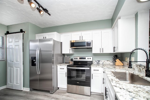 kitchen featuring appliances with stainless steel finishes, sink, light wood-type flooring, white cabinets, and track lighting