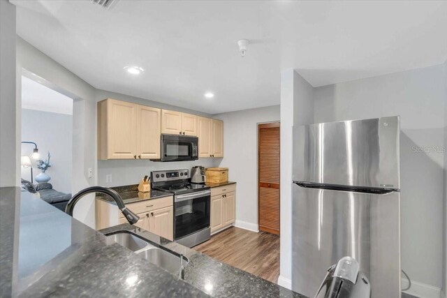 kitchen with appliances with stainless steel finishes, sink, dark stone countertops, and light hardwood / wood-style floors