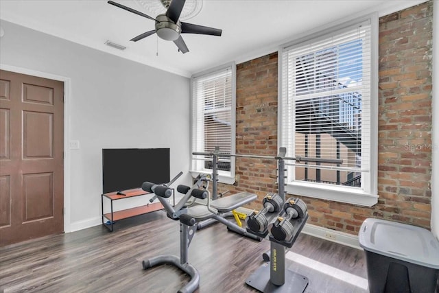 exercise area featuring ceiling fan, wood-type flooring, and brick wall