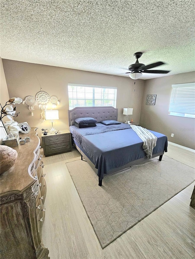 bedroom with a textured ceiling, ceiling fan, and light hardwood / wood-style flooring