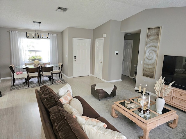 living room featuring light wood-type flooring, a textured ceiling, and vaulted ceiling