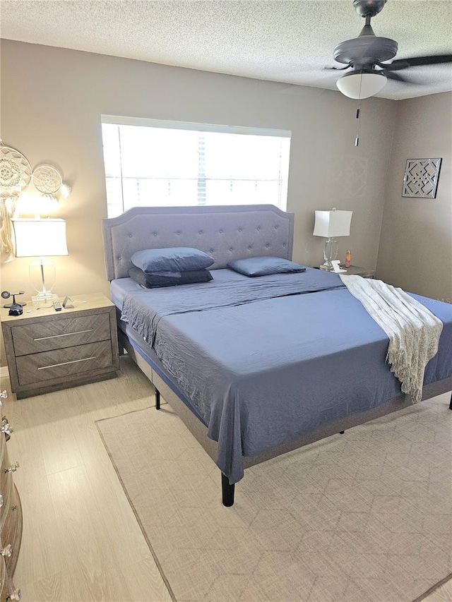 bedroom featuring ceiling fan, a textured ceiling, light hardwood / wood-style floors, and multiple windows