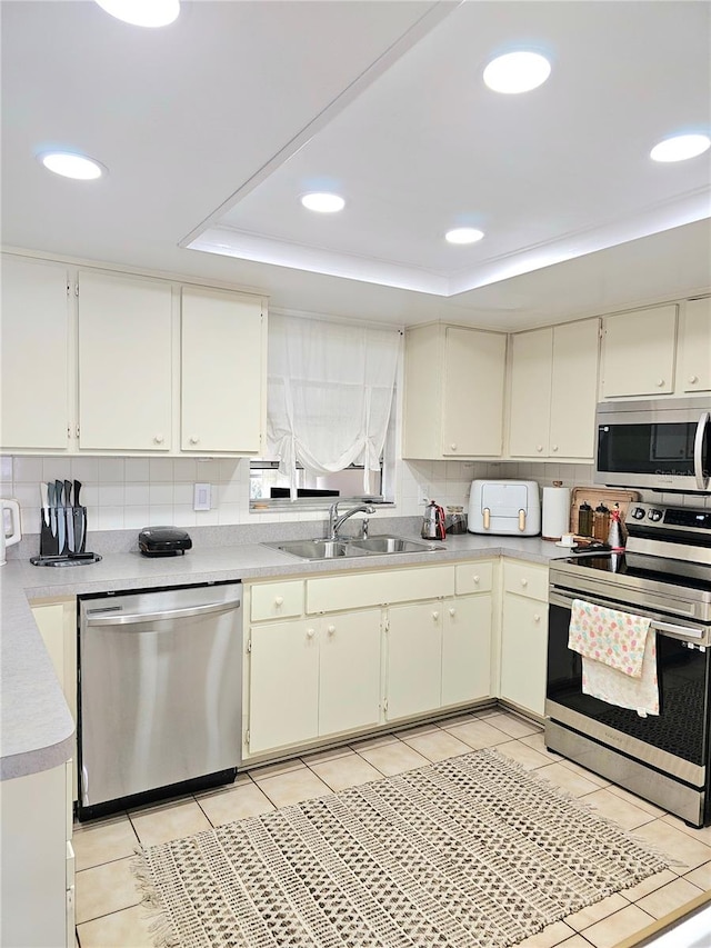 kitchen featuring a raised ceiling, appliances with stainless steel finishes, light tile patterned floors, and sink