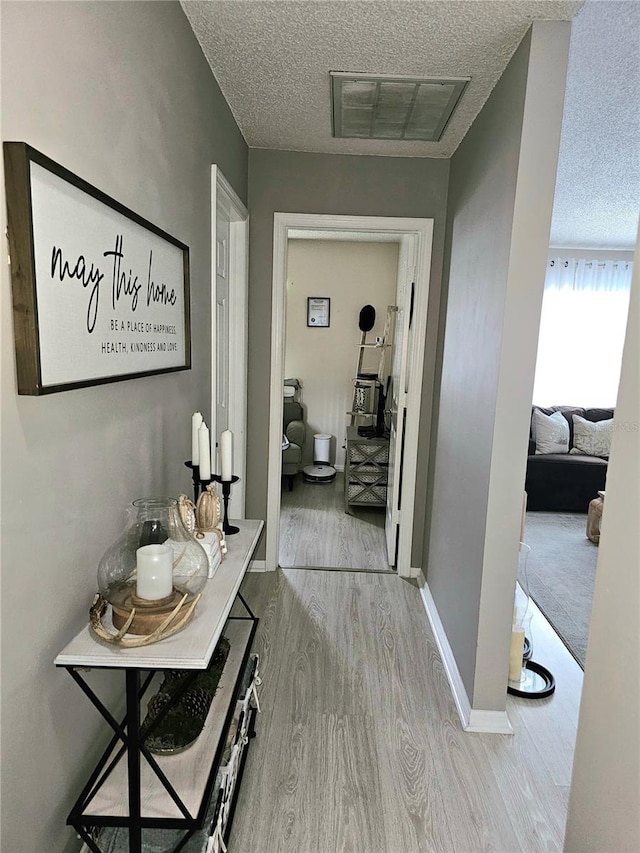 hallway with a textured ceiling and light hardwood / wood-style floors