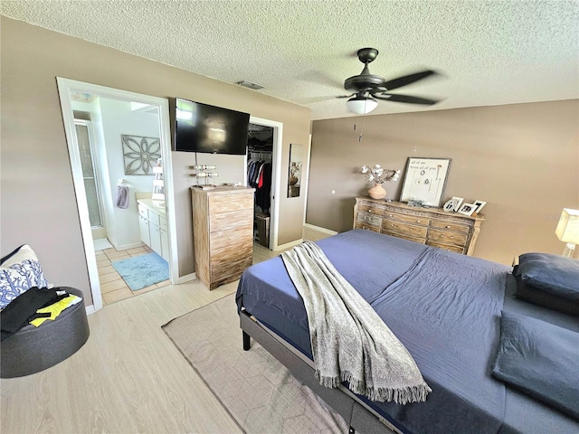 bedroom featuring ceiling fan, a textured ceiling, a closet, light wood-type flooring, and ensuite bath