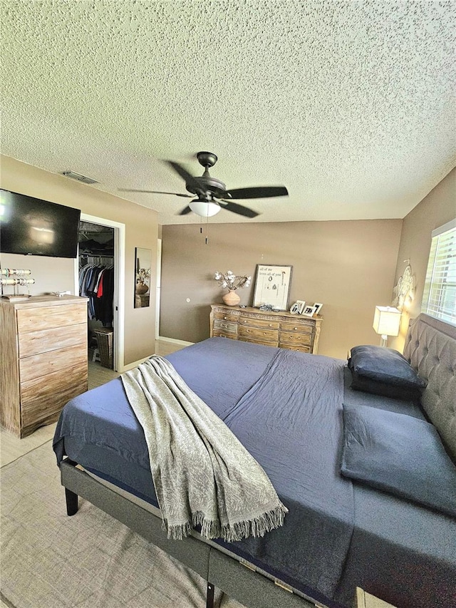 bedroom featuring a closet, a walk in closet, ceiling fan, and a textured ceiling